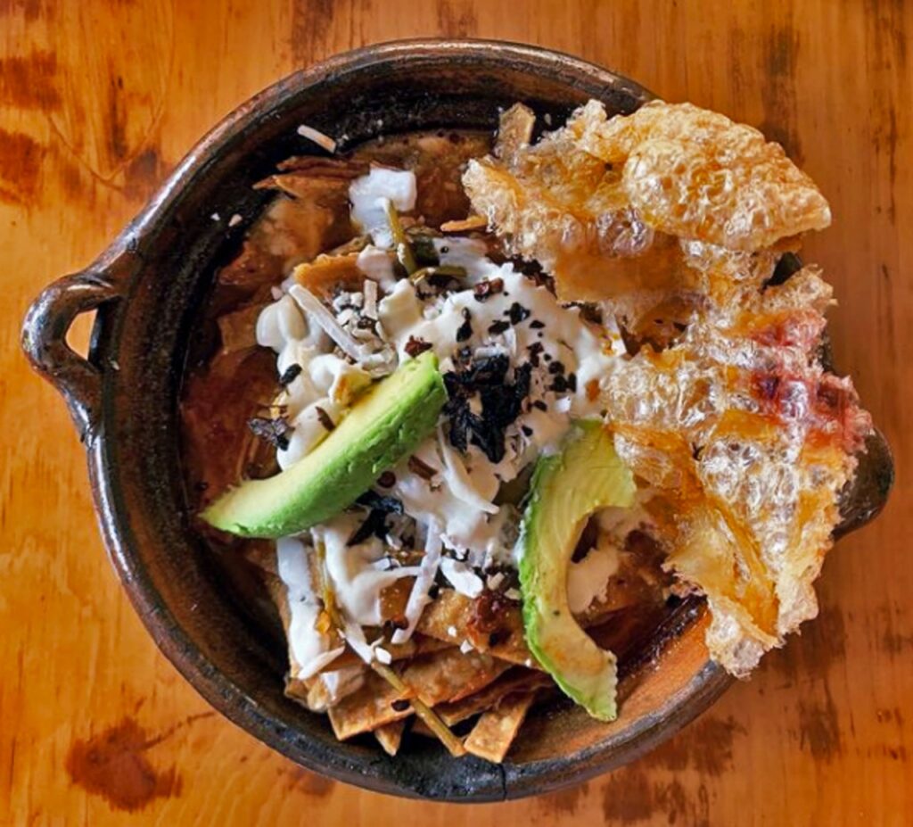 A bowl of tortilla soup, garnished with cheese, avocado, and chicharron
