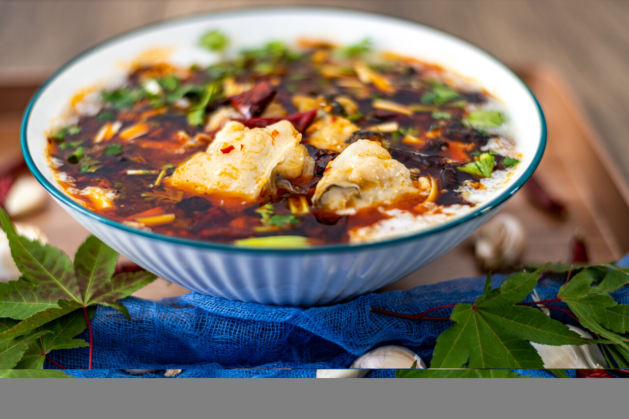 Bowl of spicy soup with fish and vegetables on wooden background