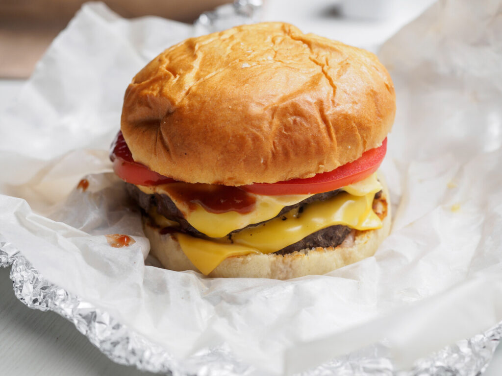 Double cheese burger with beef and tomatoes on paper