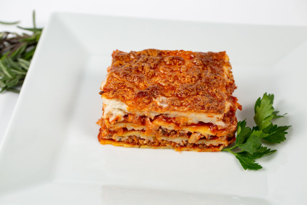 Slice of layered lasagna with meat sauce and melted mozzarella on a white plate