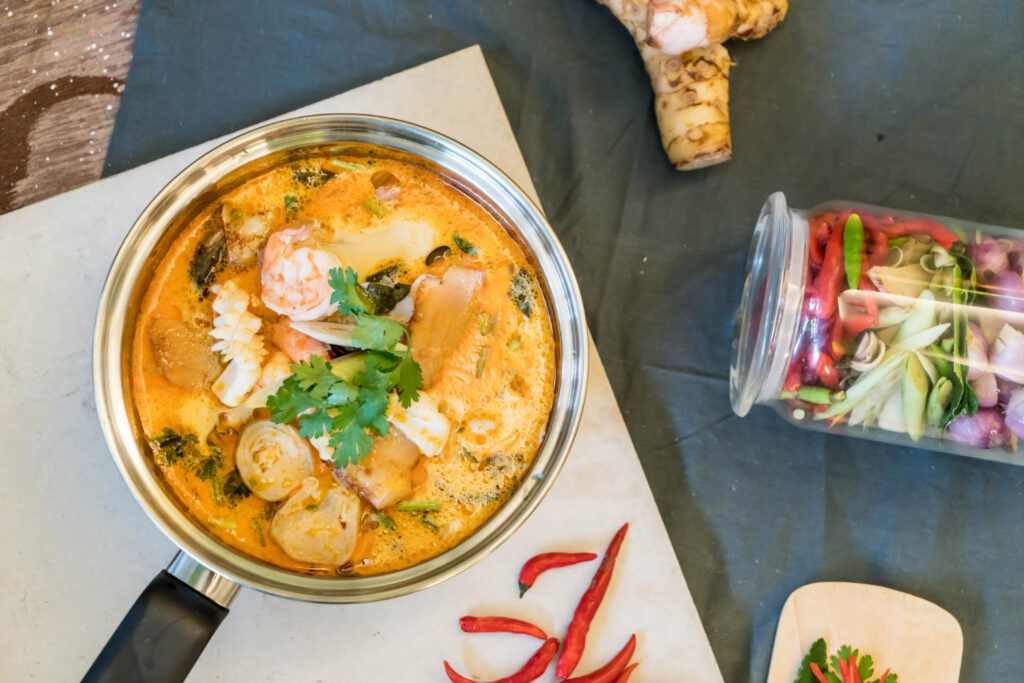 Bowl of Tom Yum soup with shrimp, herbs, and lime in a cozy restaurant setting