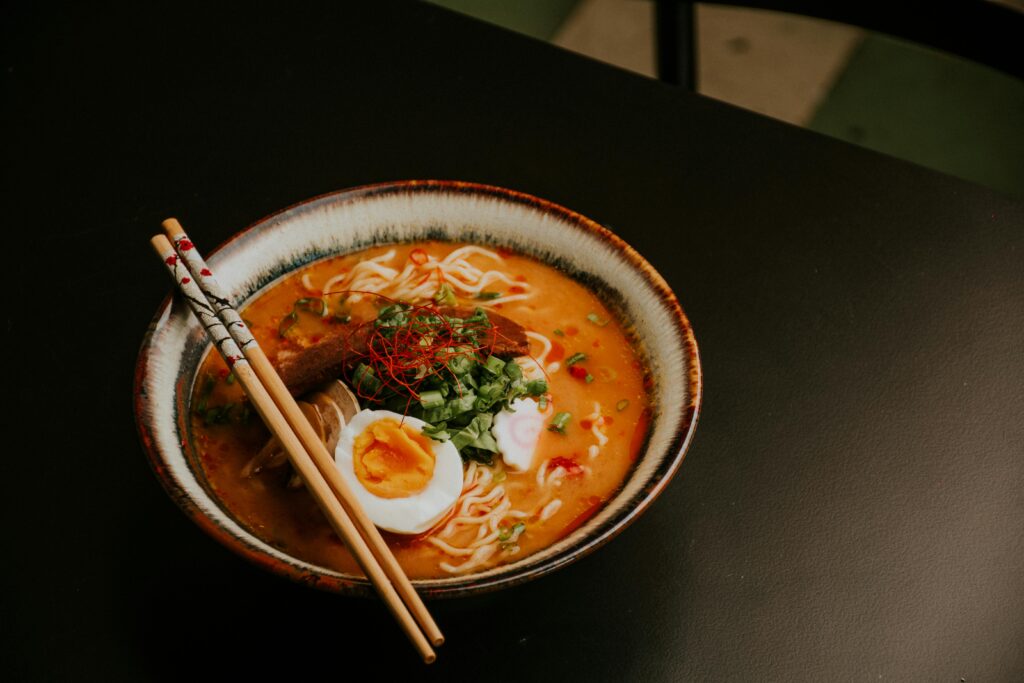 Steaming bowl of ramen noodles with broth, soft boiled egg, and green onions