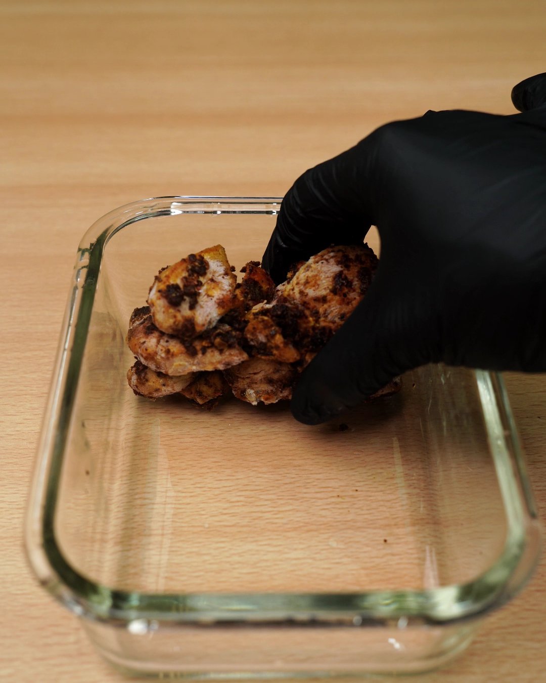 Frozen seasoned chicken pieces being placed in a glass meal prep container