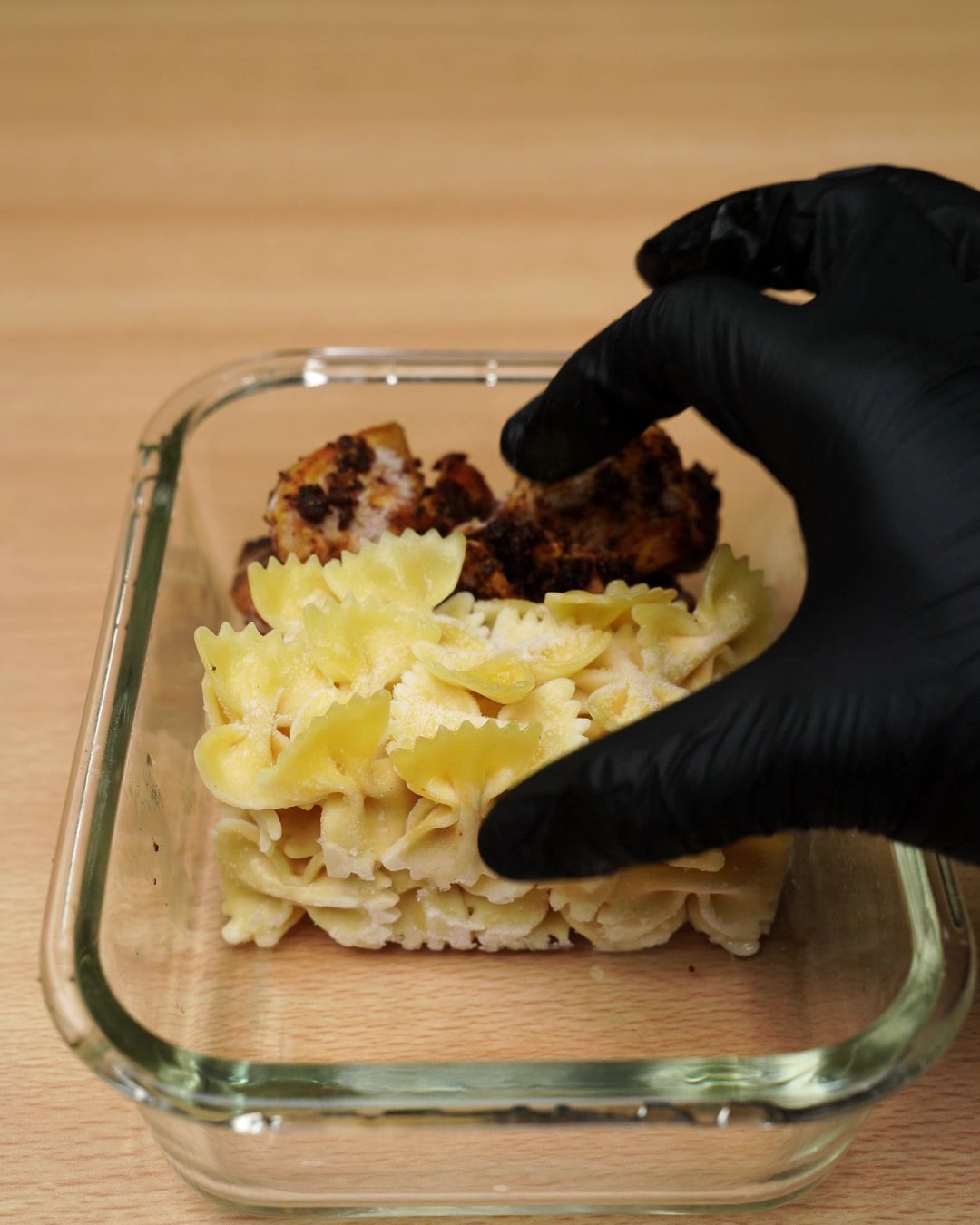 Bowtie pasta pressed into place next to the chicken in a glass meal prep box