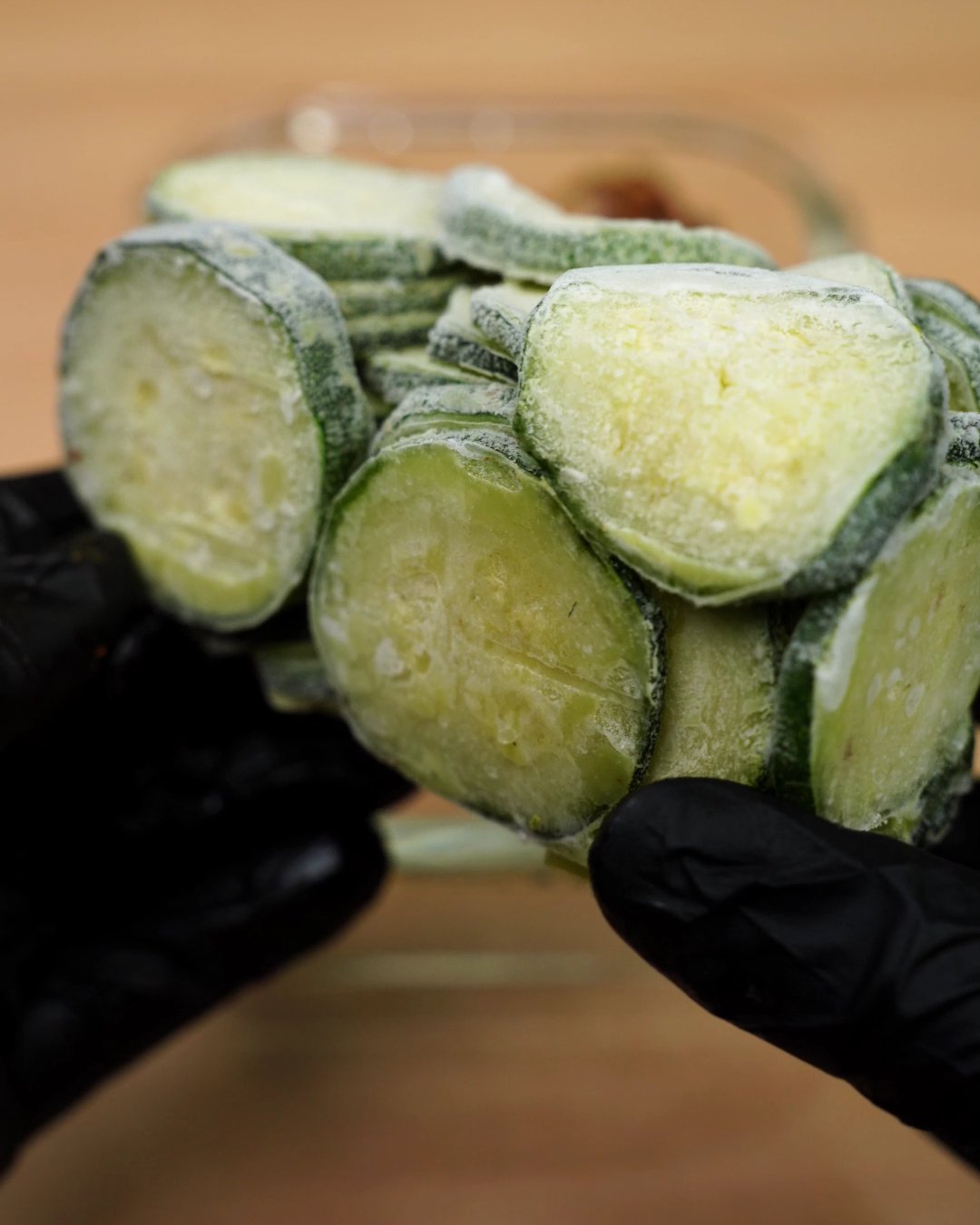 A handful of frosty frozen zucchini rounds held over the container