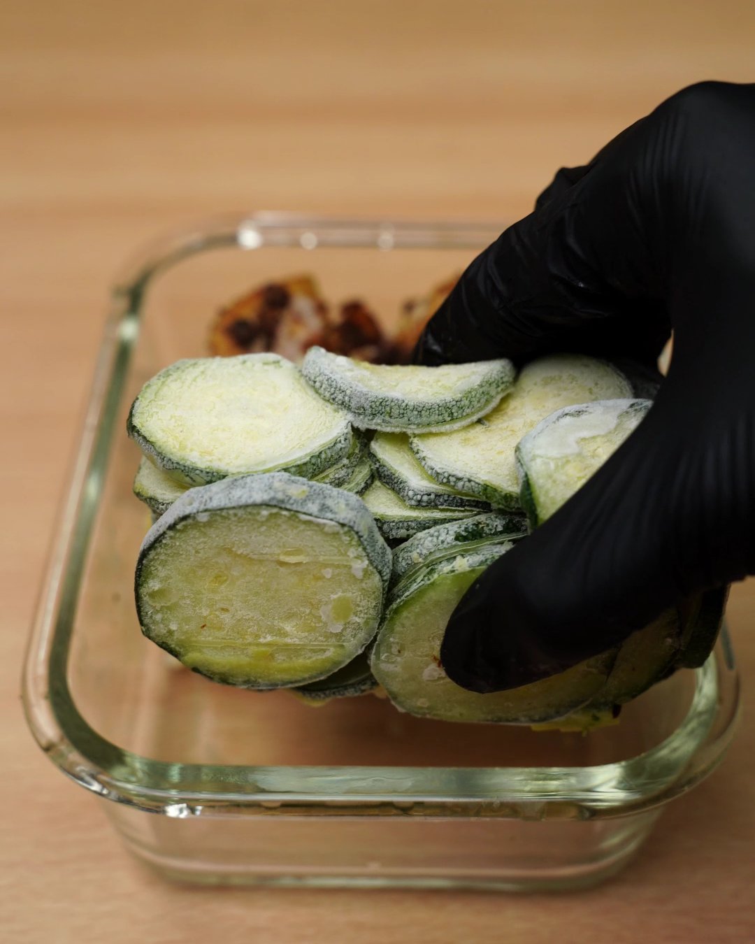 Frozen zucchini rounds being tucked into the glass container beside the pasta