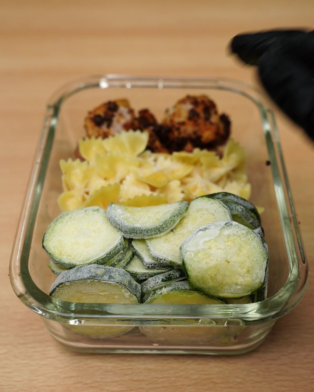 Glass freezer box packed with frozen chicken, bowtie pasta and zucchini rounds