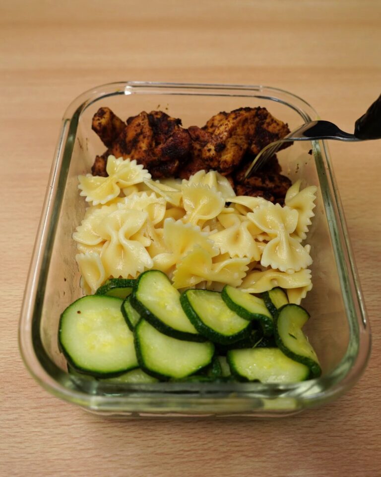 Reheated chicken, bowtie pasta and zucchini in a glass container with a fork