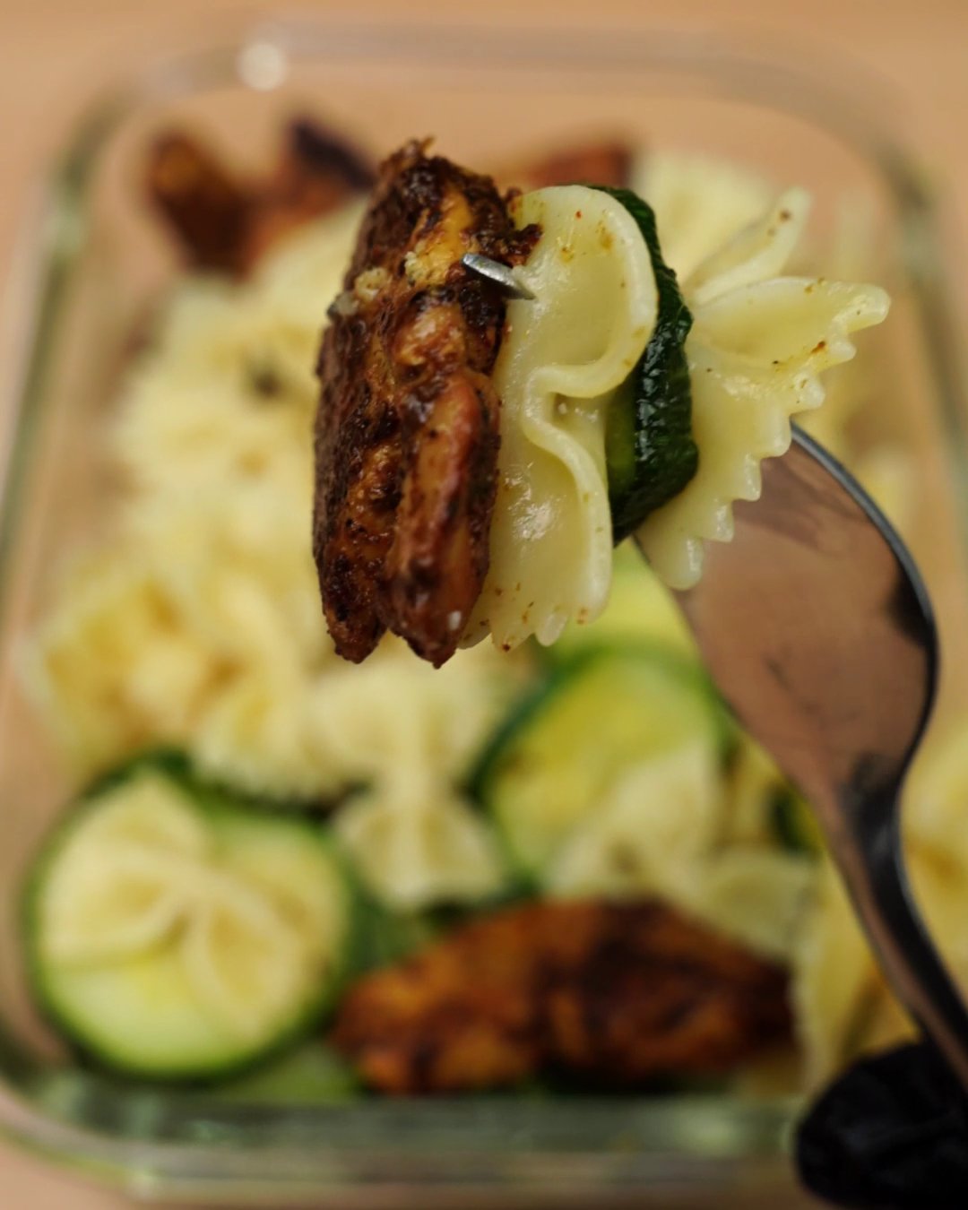 Close-up of a forkful of spiced chicken, bowtie pasta and zucchini