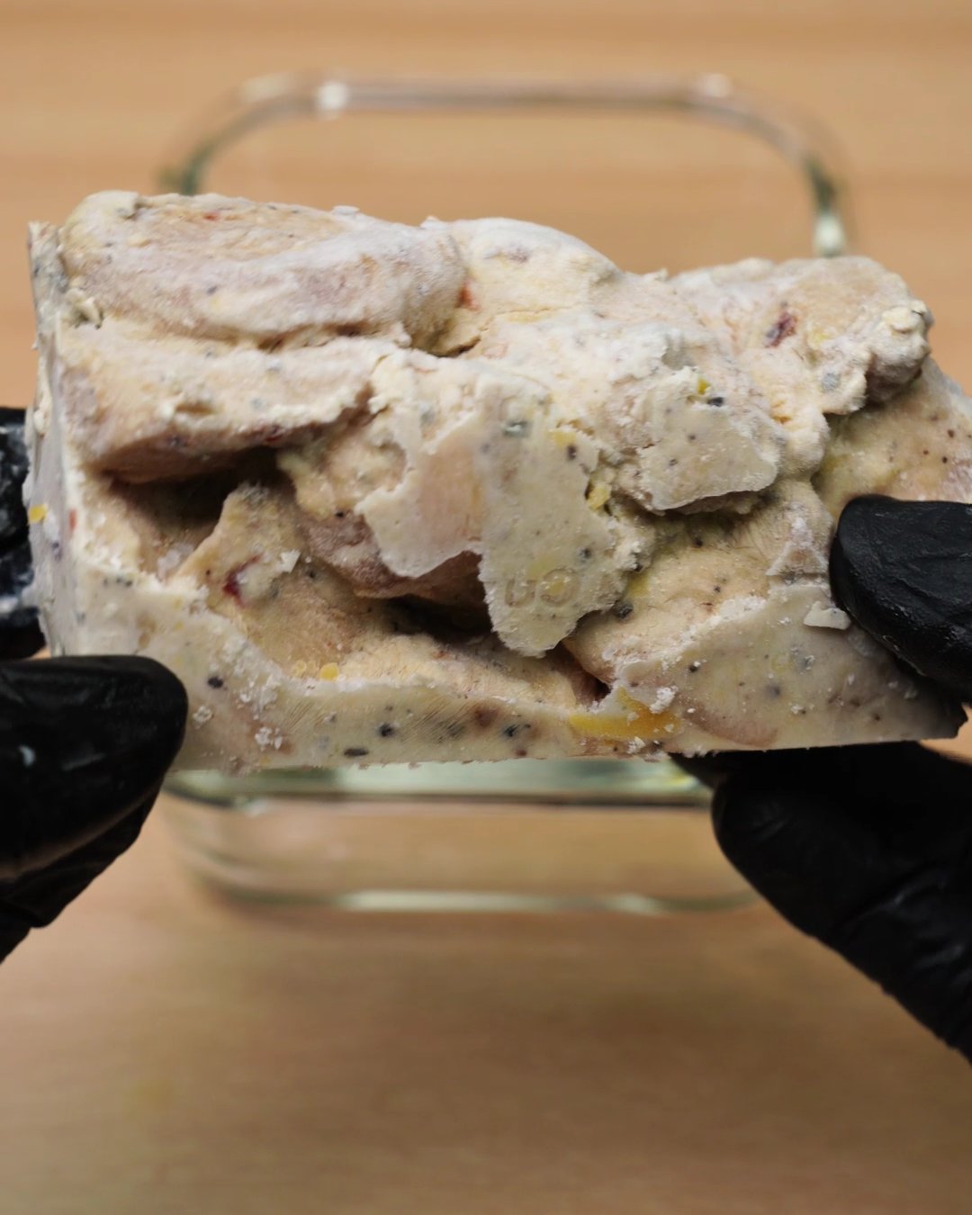 Gloved hands holding a frozen block of creamy chicken slices over a glass dish