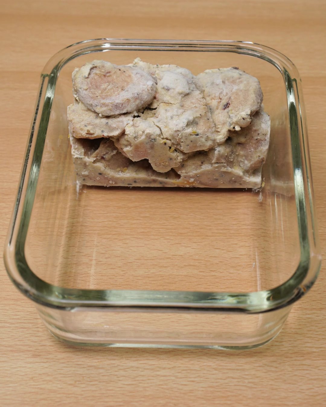 Frozen creamy chicken block placed in the end of a glass meal prep dish