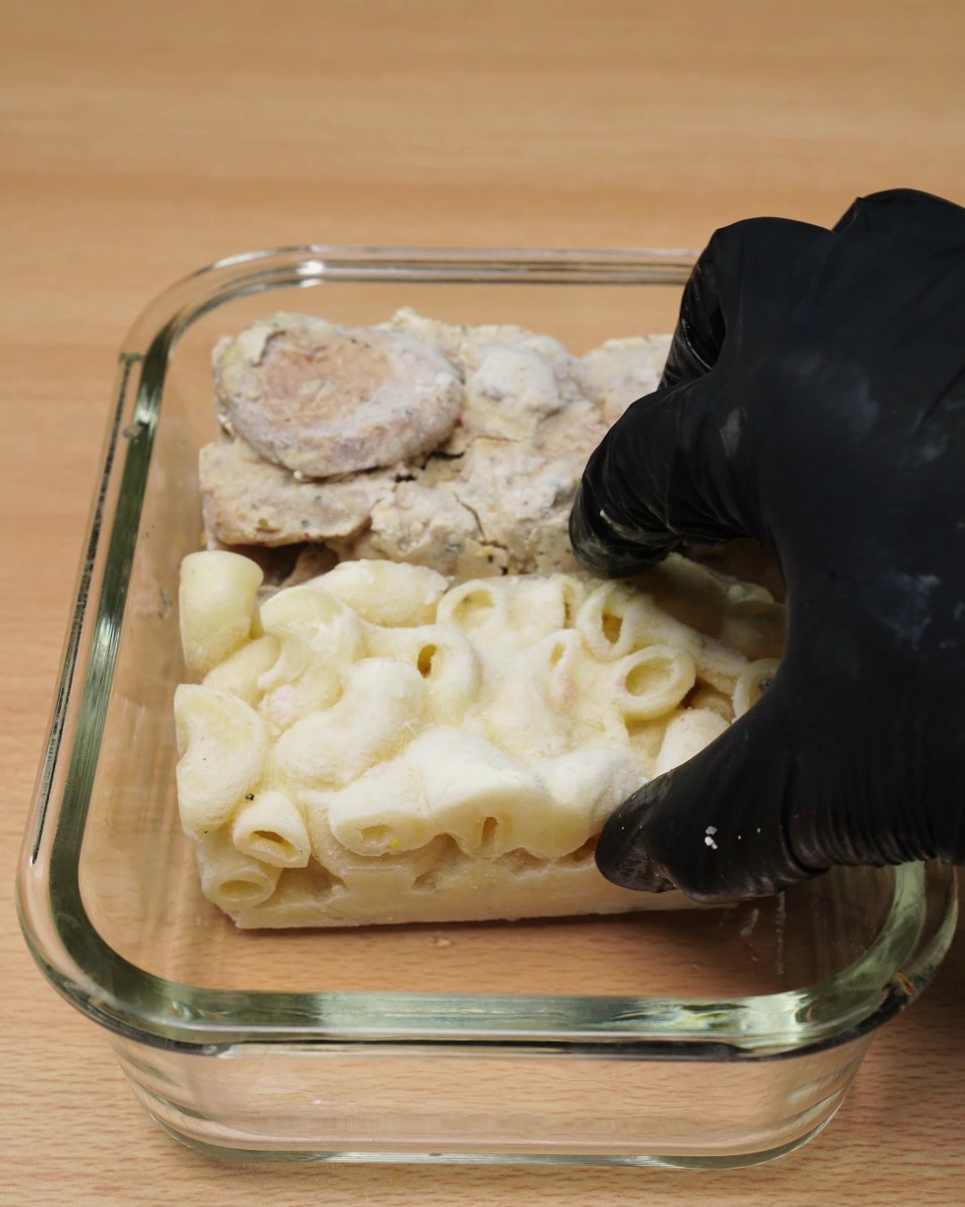 Frozen macaroni and cheese sauce block being placed next to the chicken in a glass dish