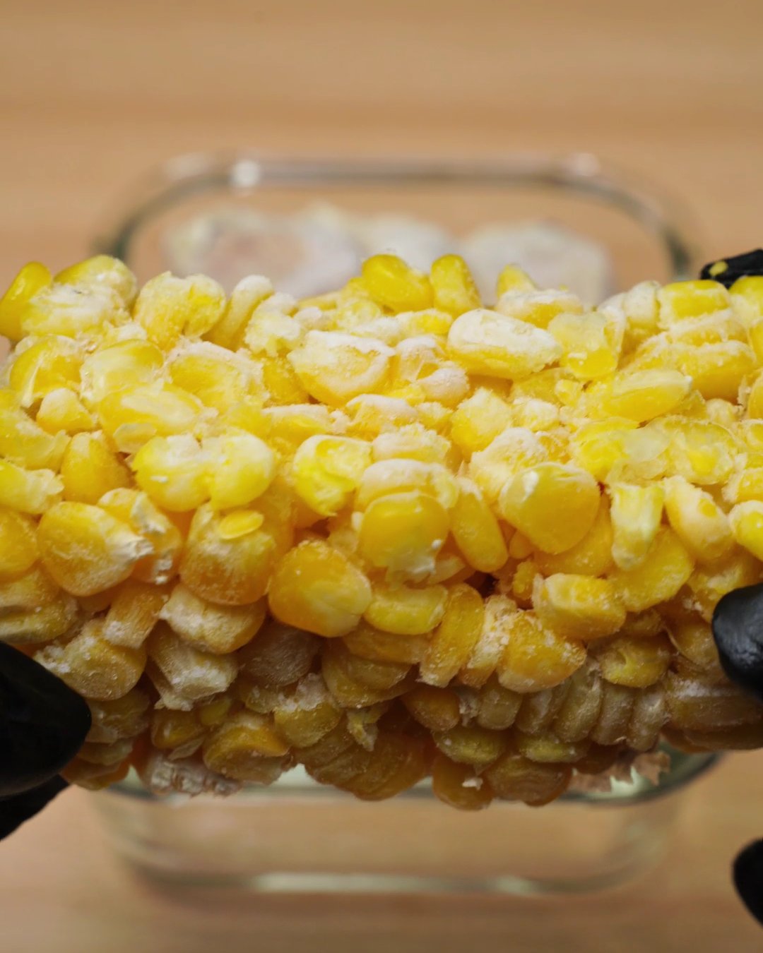 Frozen sweet corn block being held over a glass dish