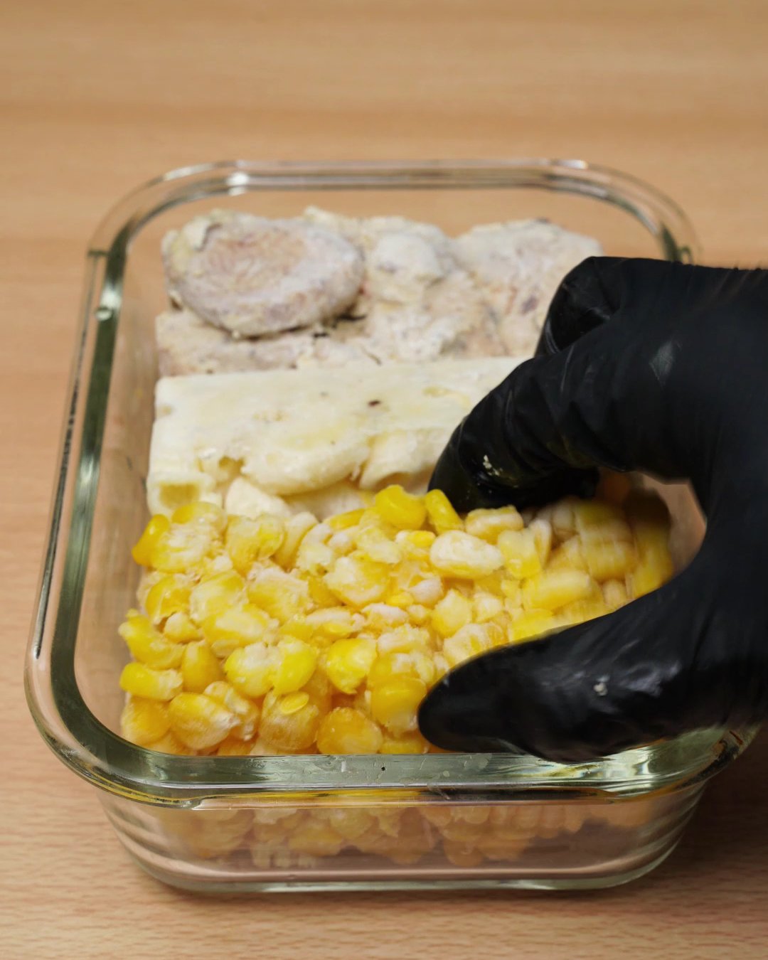 Frozen corn block being pressed into a glass dish beside the chicken and macaroni