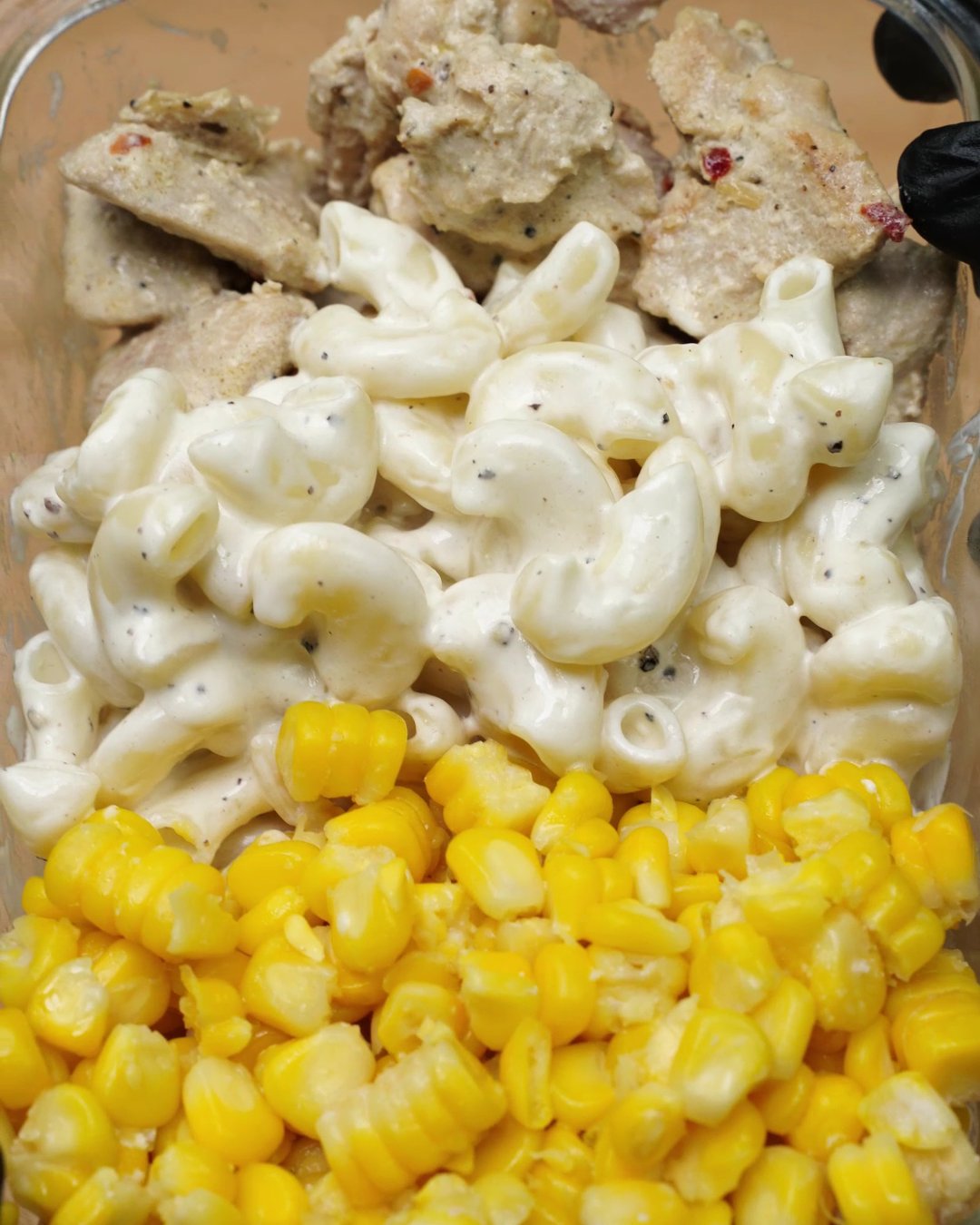 Reheated creamy chicken, macaroni and sweet corn sitting side by side in a glass dish
