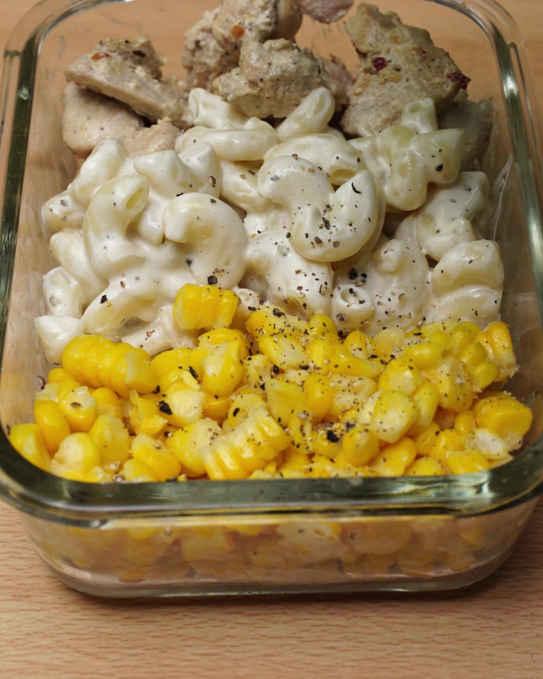 Cracked black pepper scattered over hot creamy chicken, macaroni and corn in a glass dish