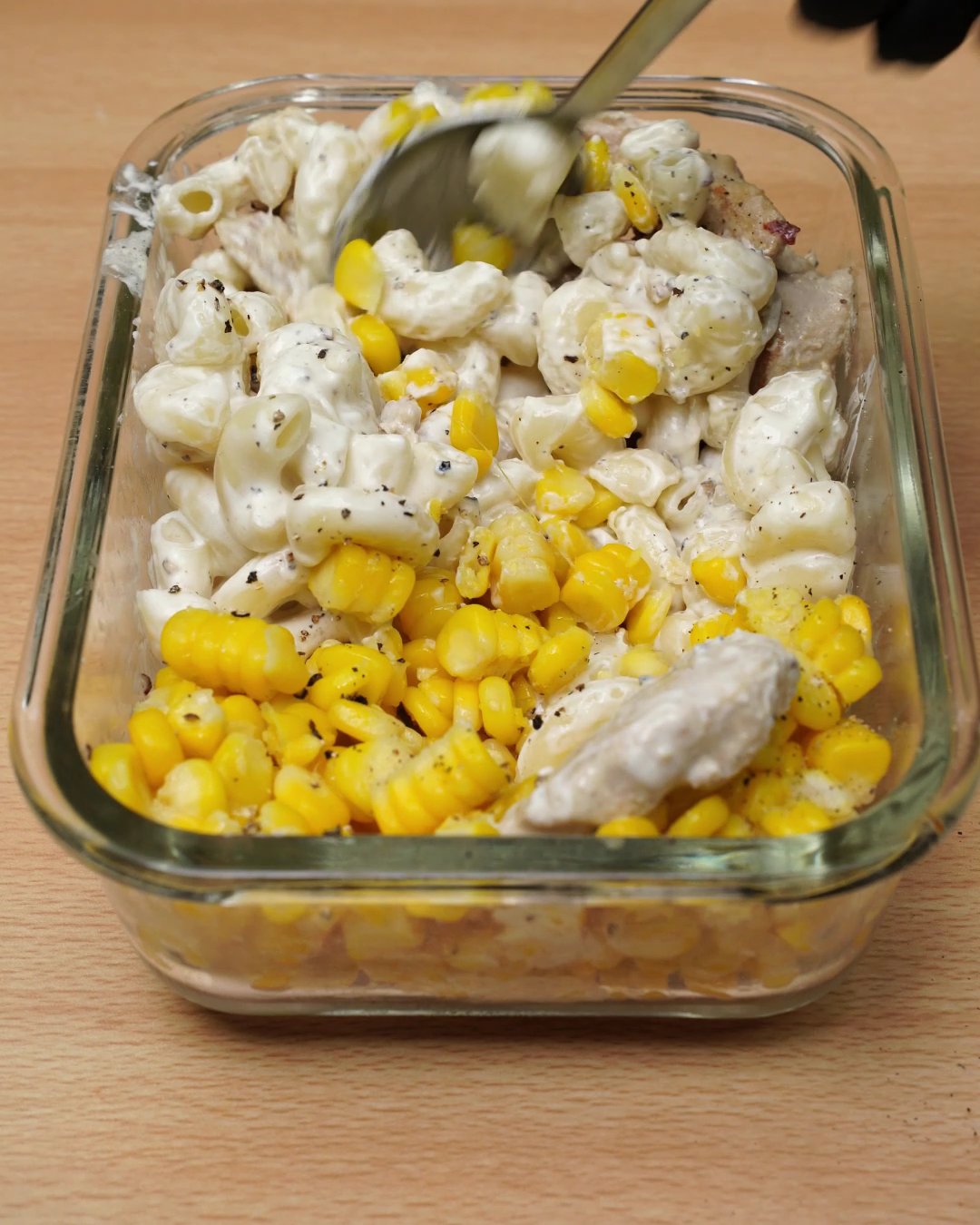 Spoon stirring the macaroni, corn and creamy chicken together in a glass dish