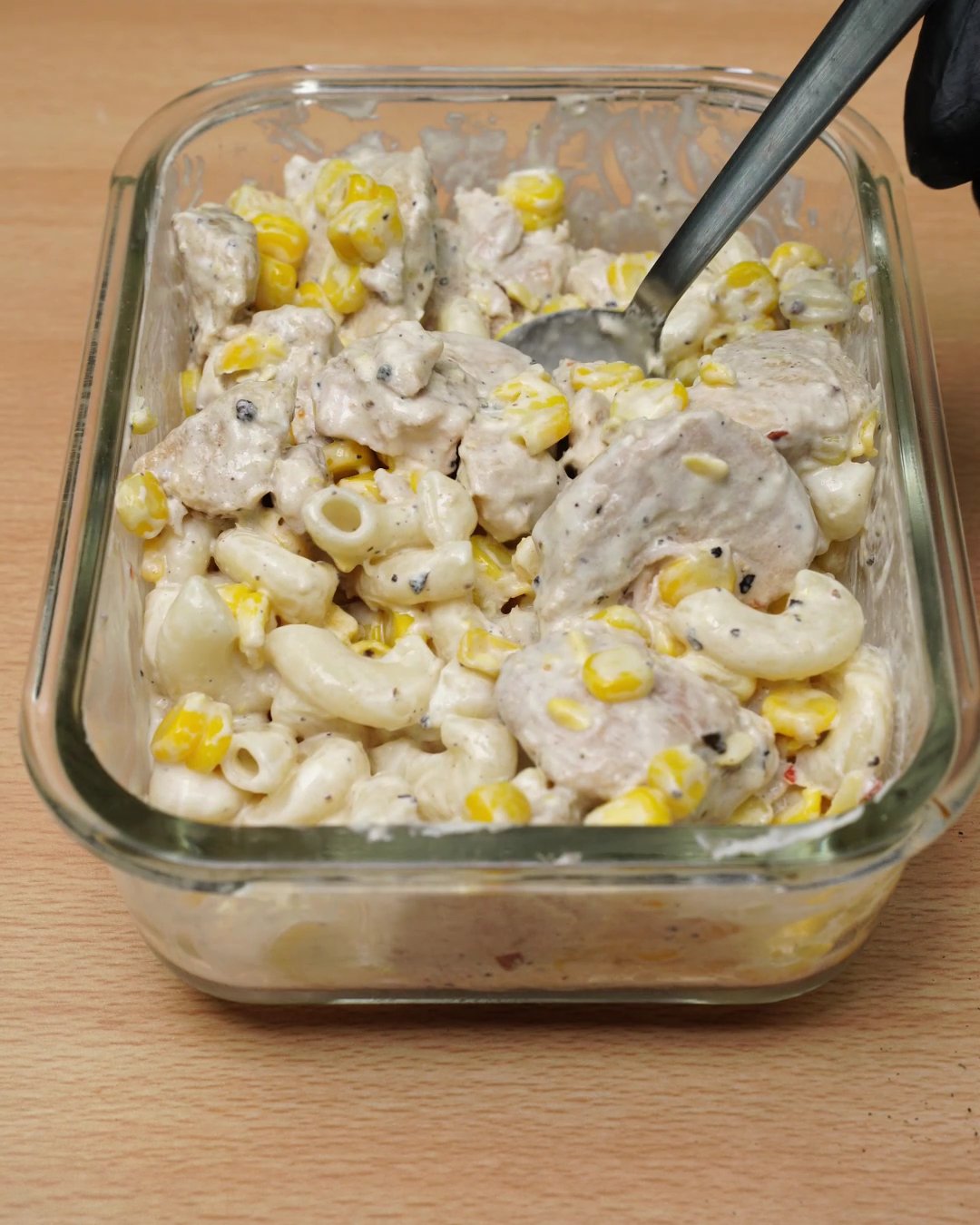 Creamy chicken and corn mac stirred together in a glass meal prep dish