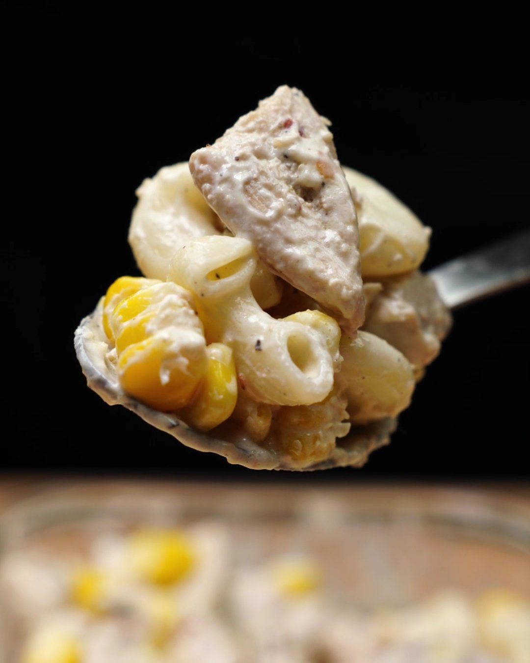 Spoonful of creamy macaroni with sweet corn and a piece of chicken
