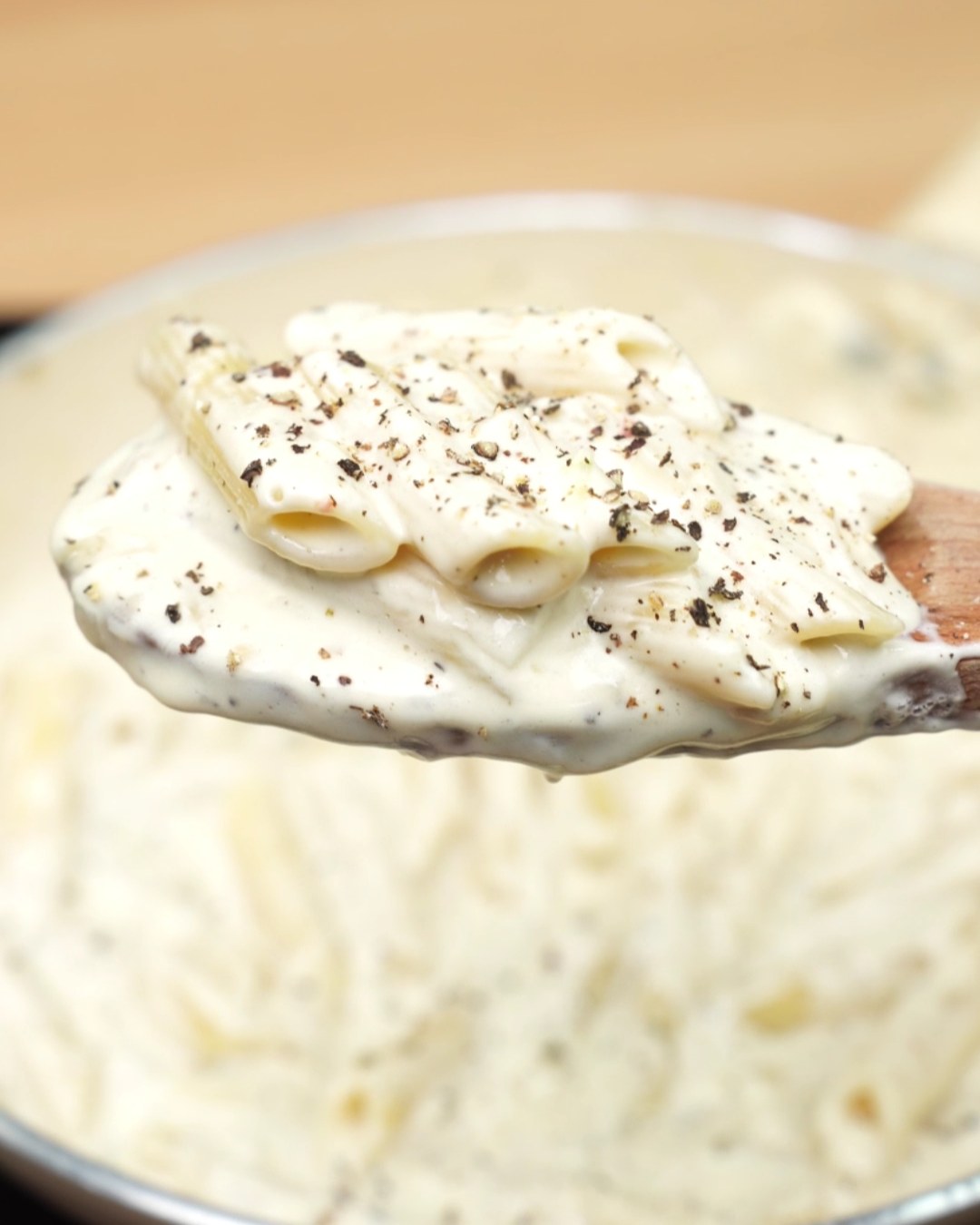 Creamy garlic Parmesan penne on a wooden spoon, topped with cracked black pepper