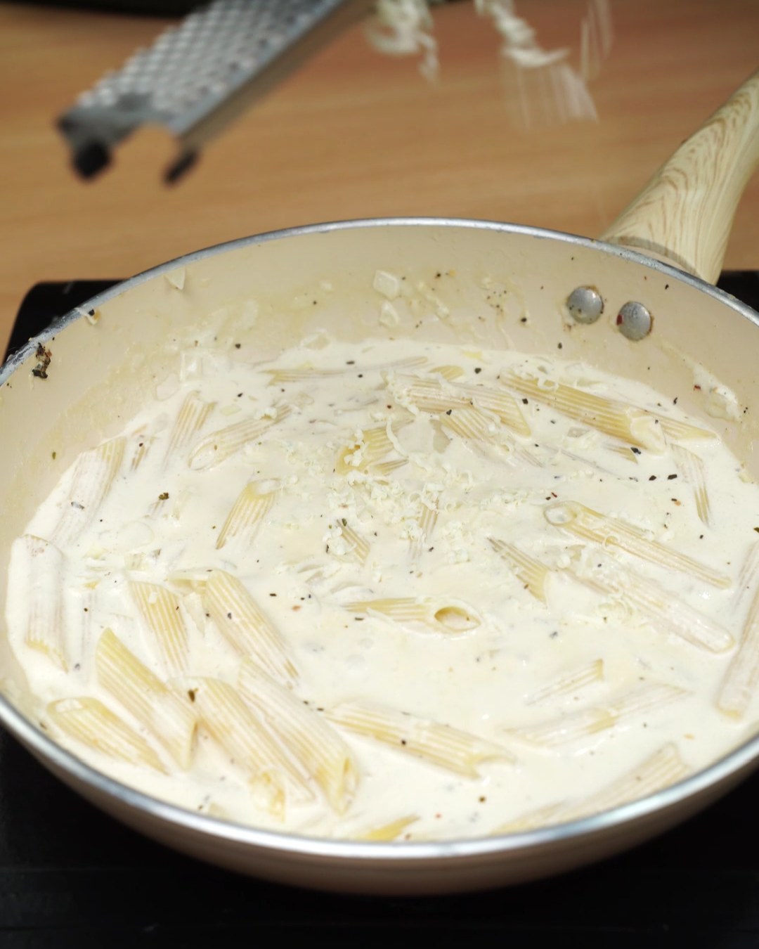 Grating Parmesan over creamy garlic penne