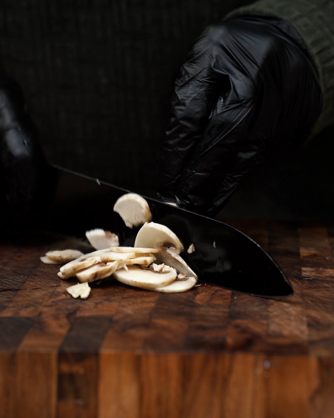 Fresh white mushrooms being sliced with a chef's knife on a wooden cutting board