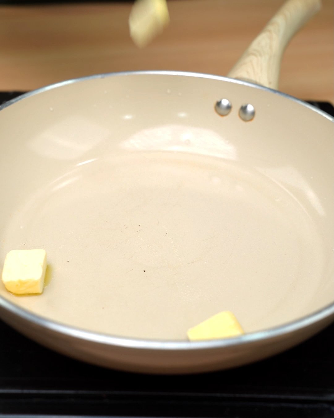 Cubes of butter melting in a cream-colored skillet