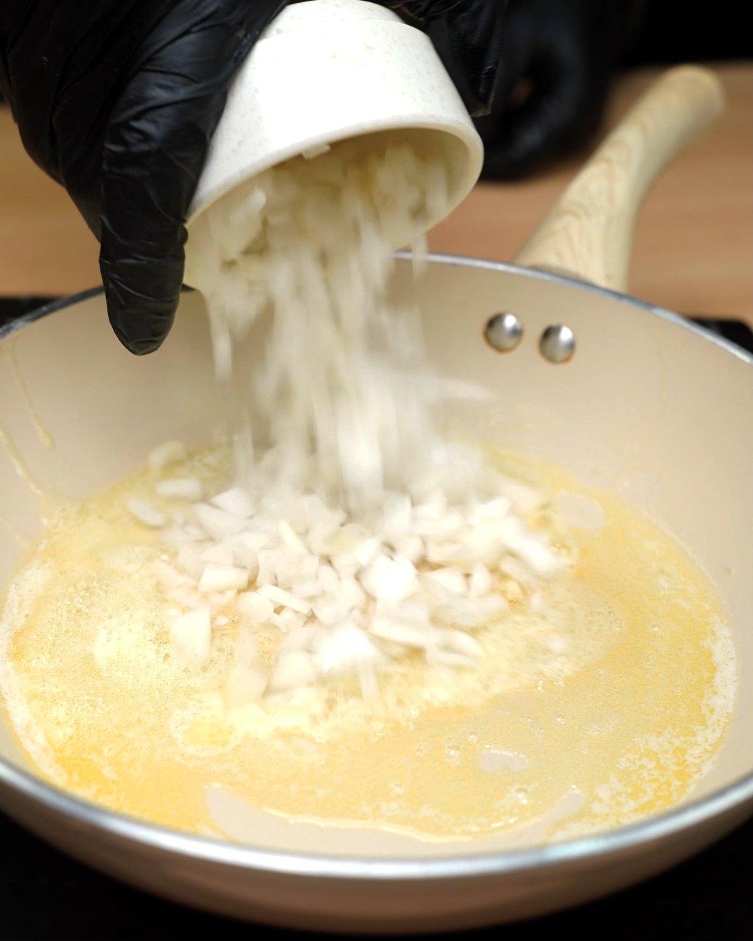 Diced onion being tipped into melted butter in a skillet