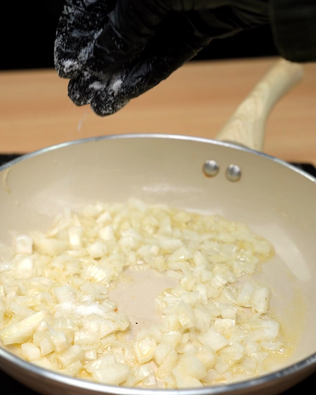 A pinch of salt being sprinkled over diced onion cooking in butter