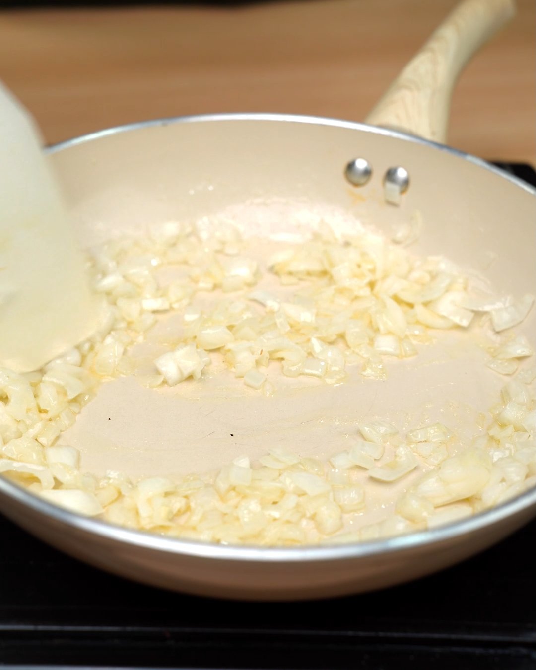 Softened diced onion being stirred in butter with a wooden spatula