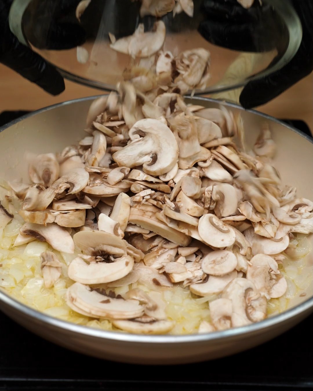 Sliced mushrooms being added to softened onion in a skillet