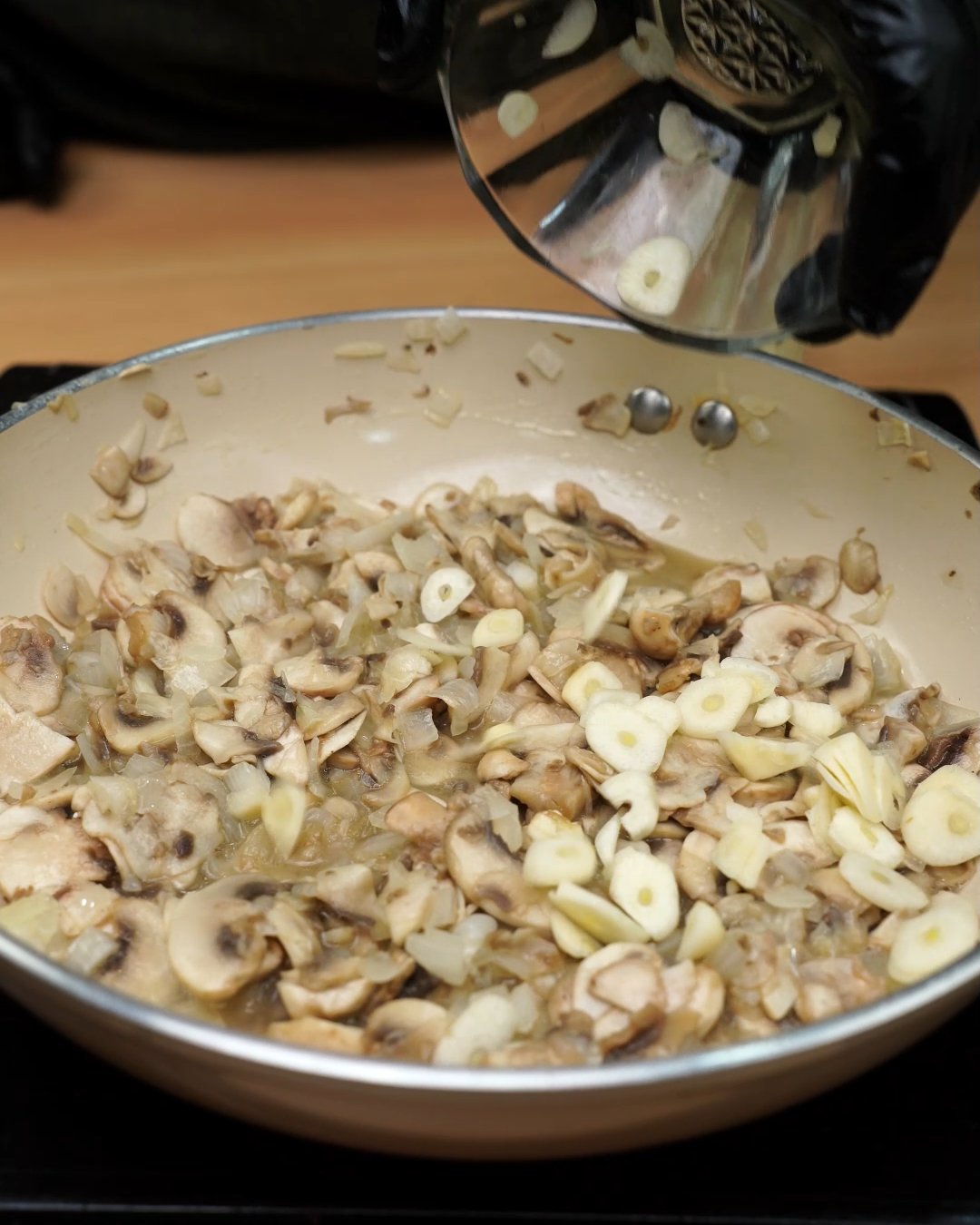 Sliced garlic being added to sautéed mushrooms and onion