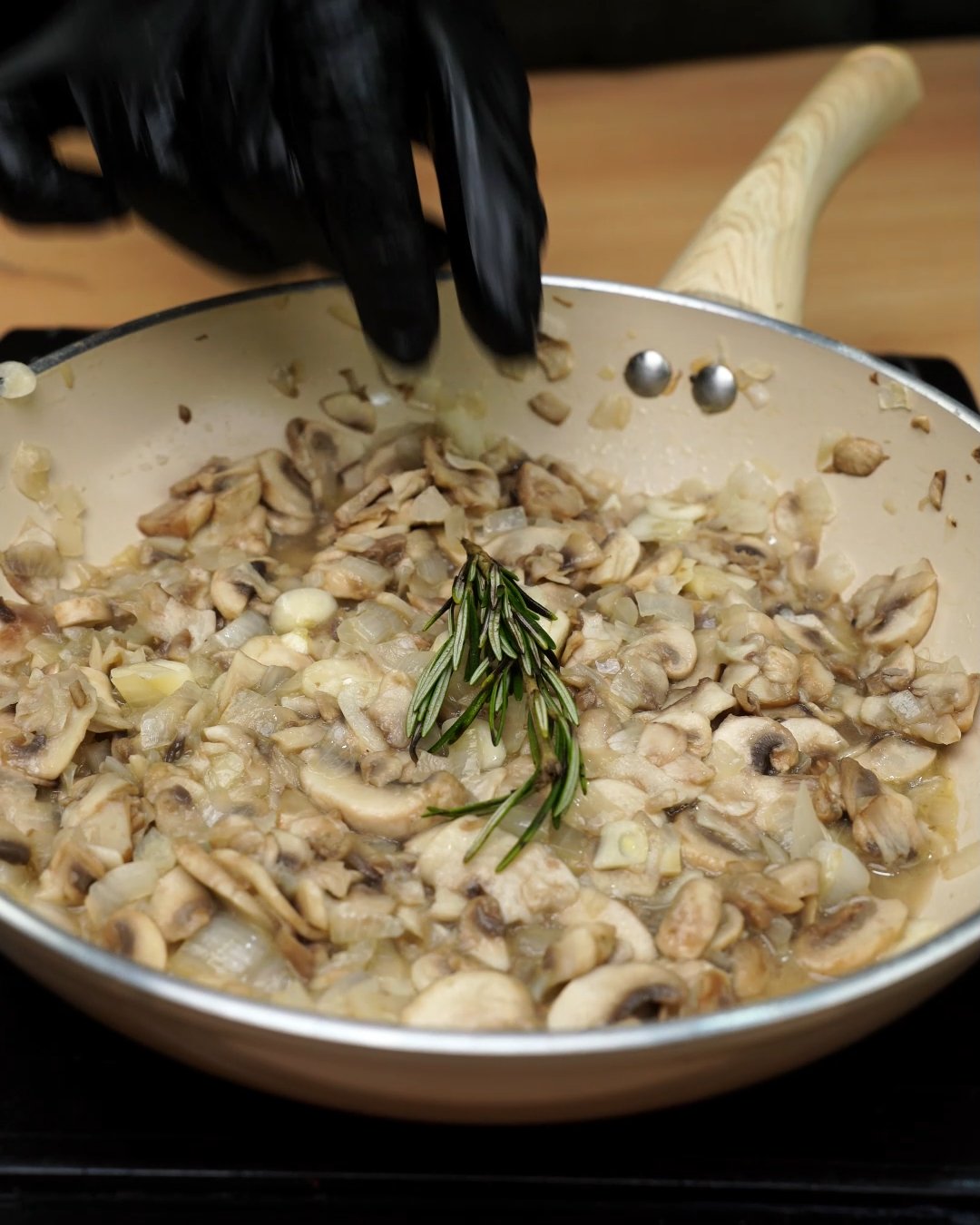 A sprig of fresh rosemary added to sautéed mushrooms in a skillet