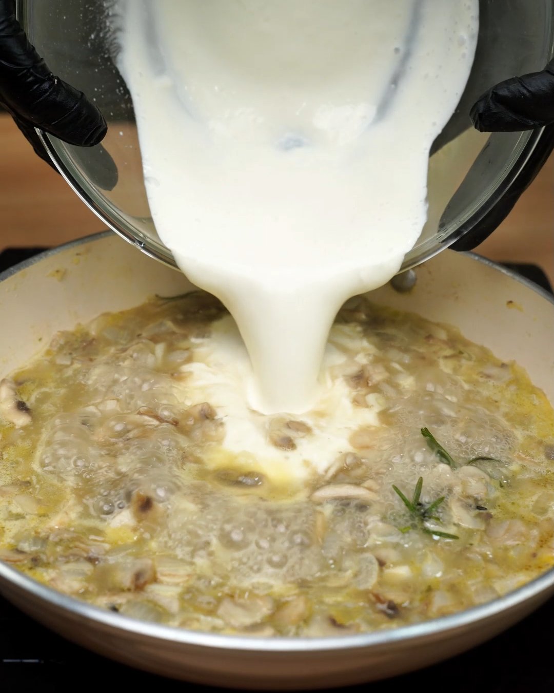 Heavy cream being poured into simmering mushroom broth