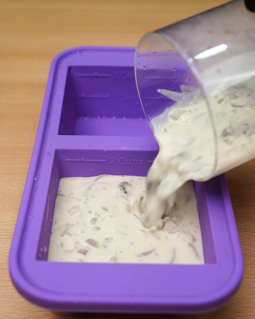 Creamy mushroom sauce being poured into a purple silicone freezer mold