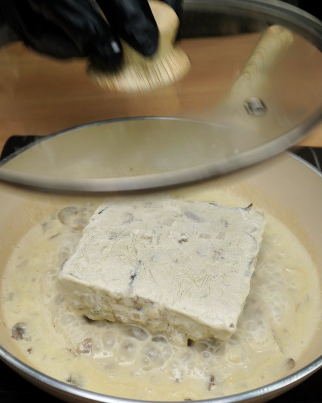 A glass lid going onto a skillet as the frozen sauce block starts to melt