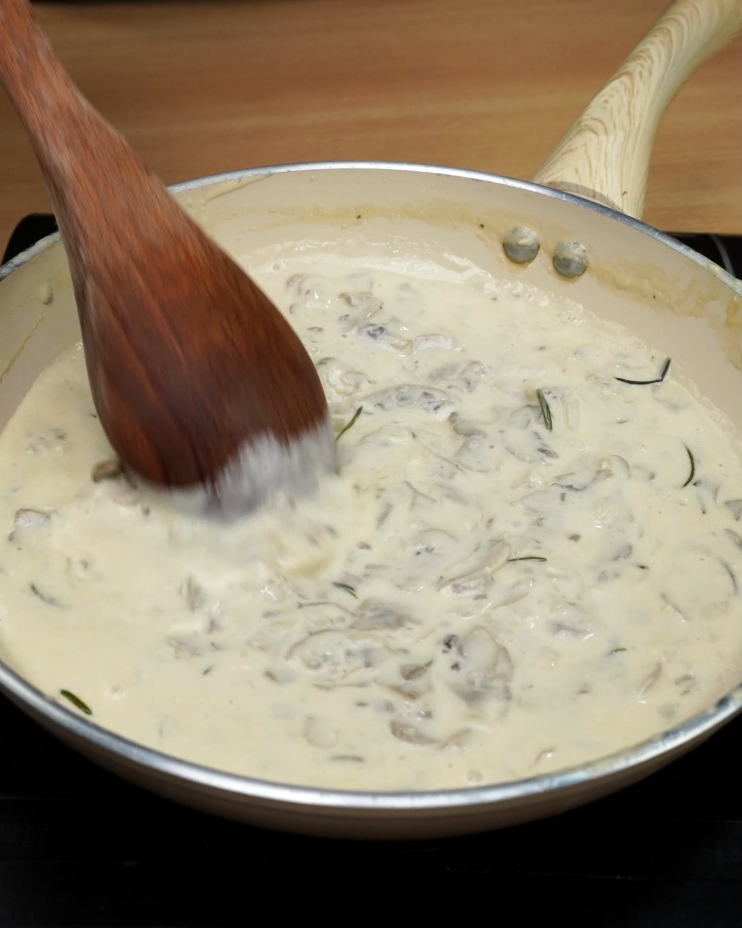 Reheated creamy mushroom sauce being stirred with a wooden spoon