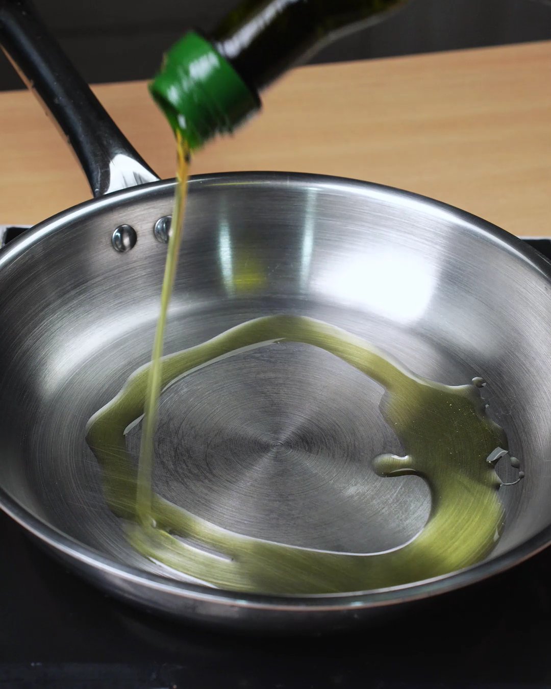 Olive oil being poured into a stainless steel skillet