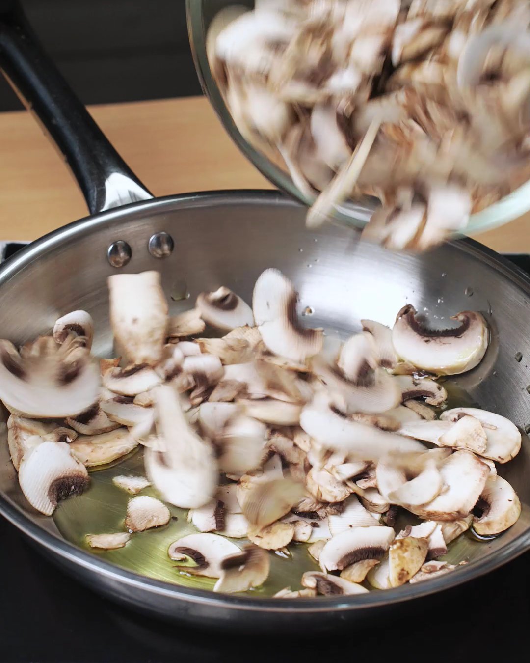 Sliced mushrooms being tipped into hot olive oil in a skillet