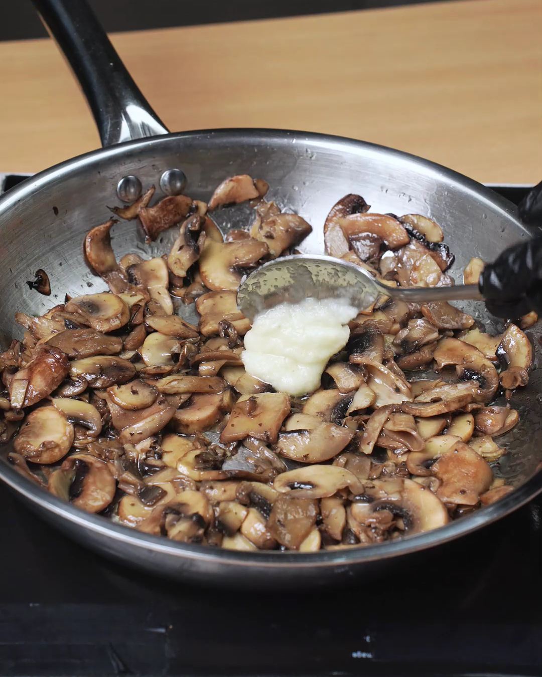 A spoonful of garlic paste added to browned mushrooms in a skillet
