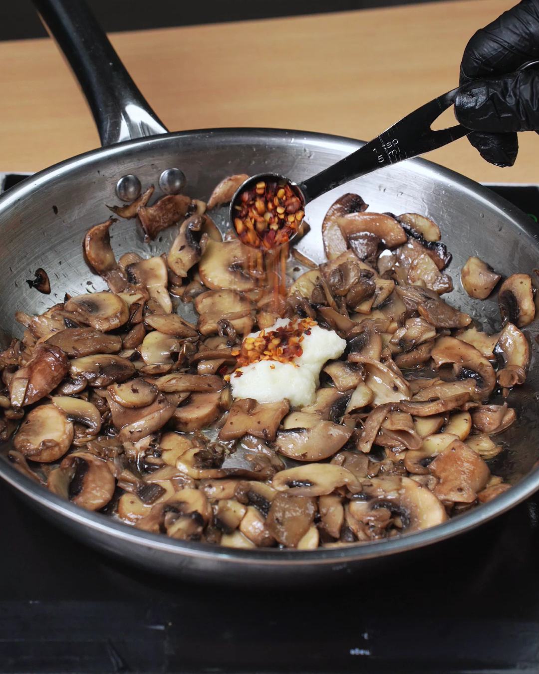 Crushed red pepper flakes being added to browned mushrooms and garlic