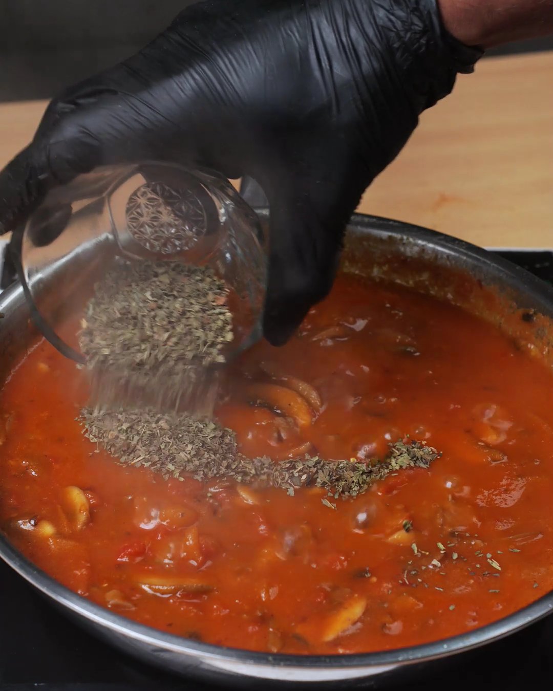 Dried Italian herbs being sprinkled over mushroom tomato sauce