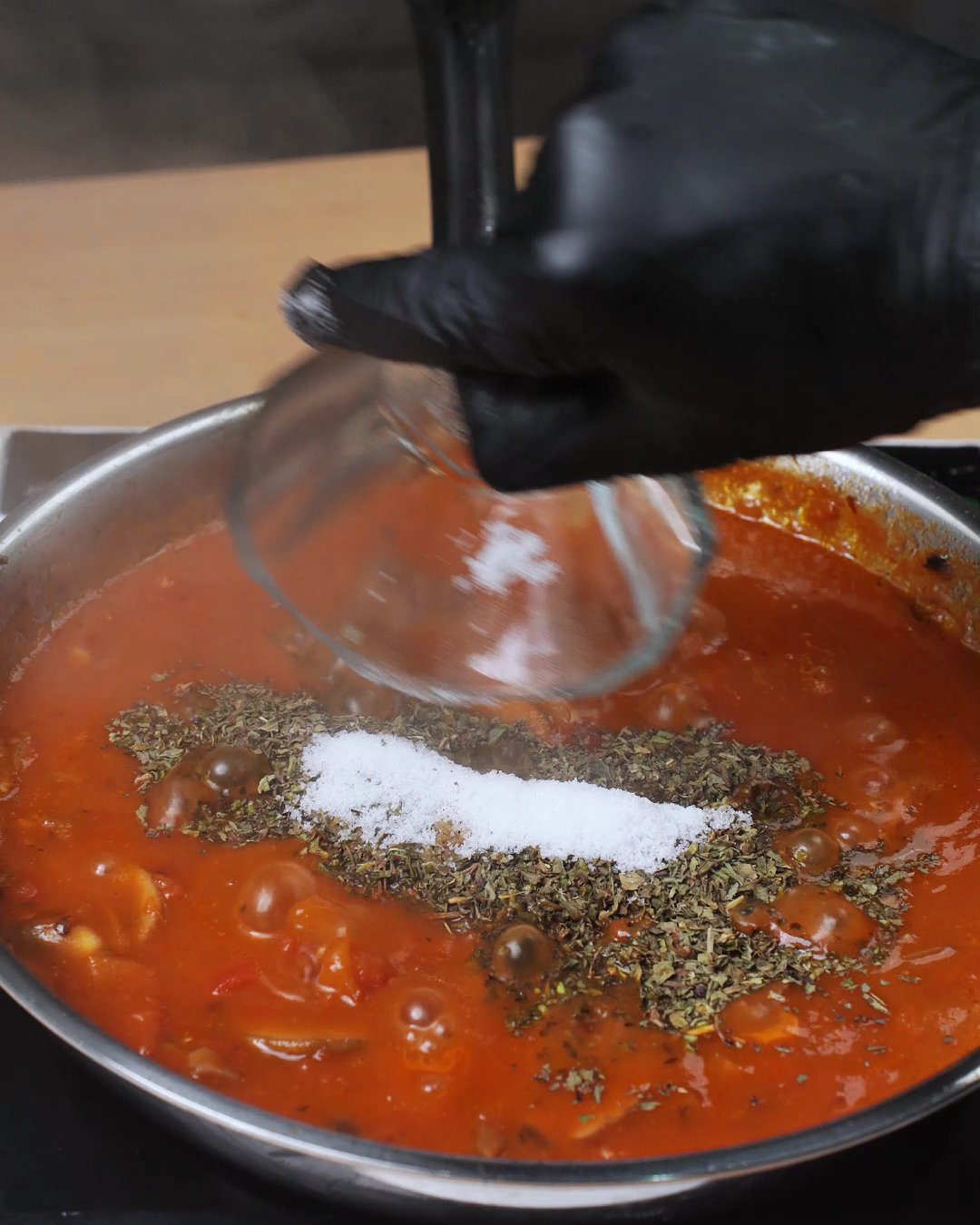 Salt being added to tomato sauce topped with dried herbs