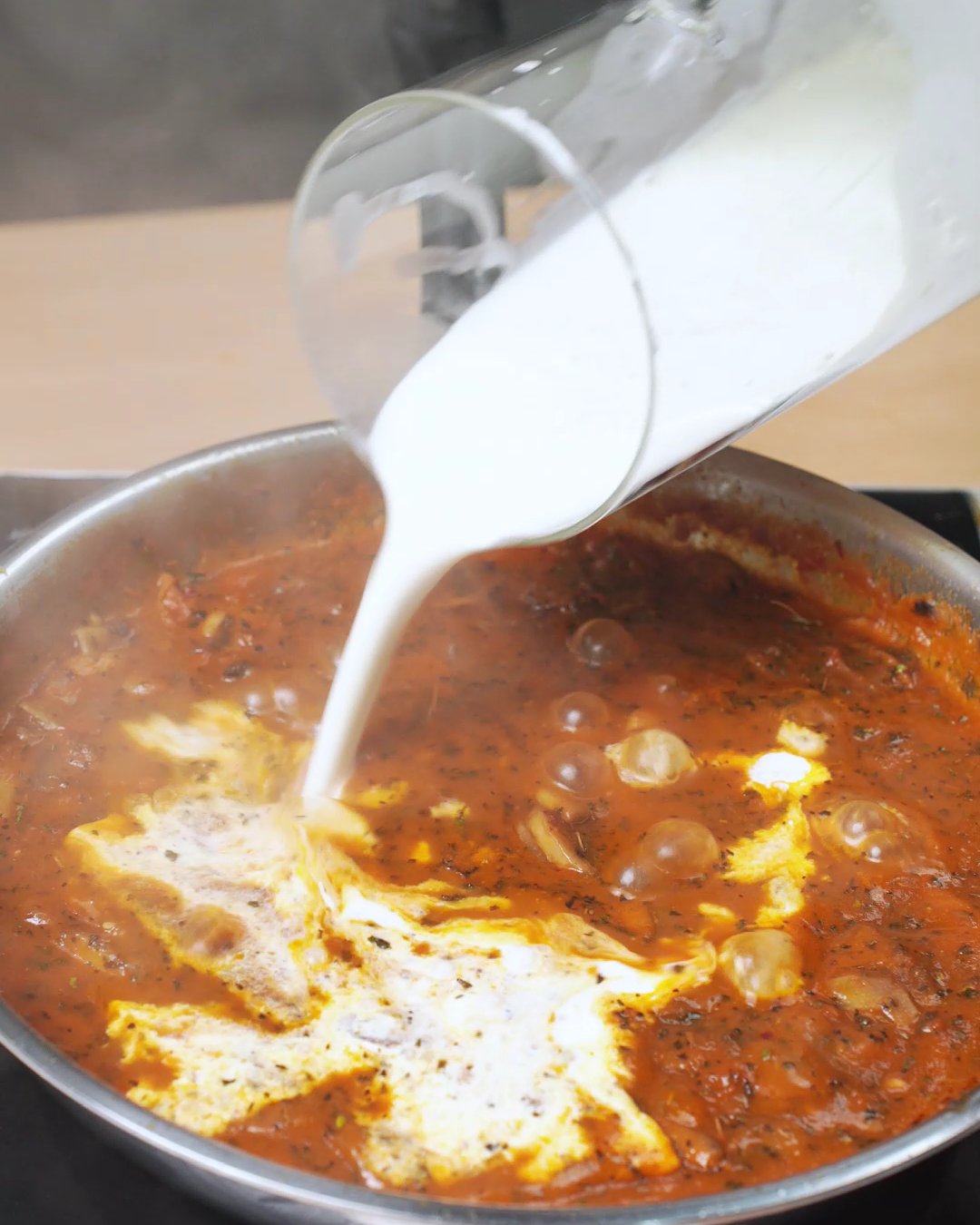 Heavy cream being poured into simmering mushroom tomato sauce