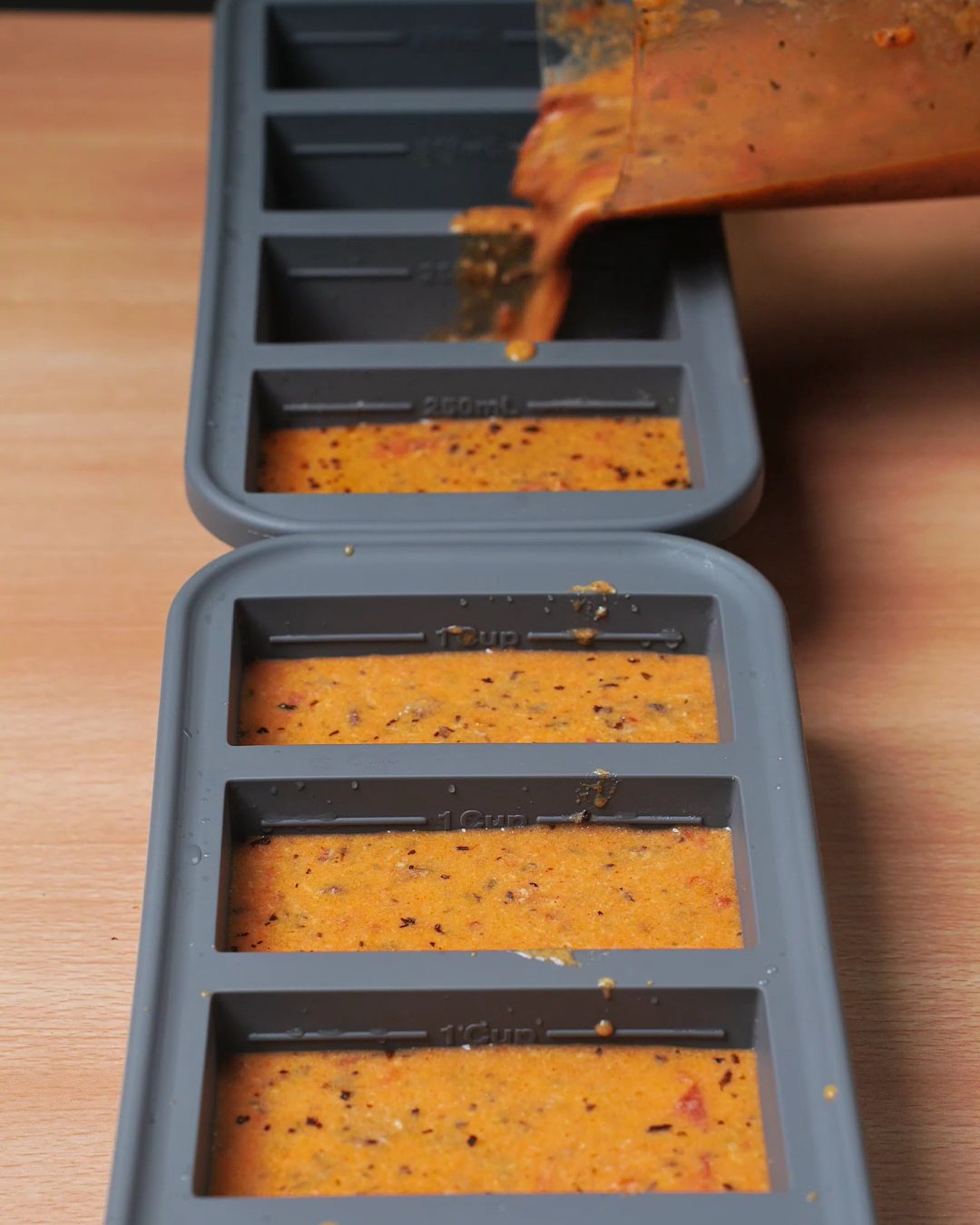 Creamy tomato mushroom sauce being poured into gray silicone freezer molds