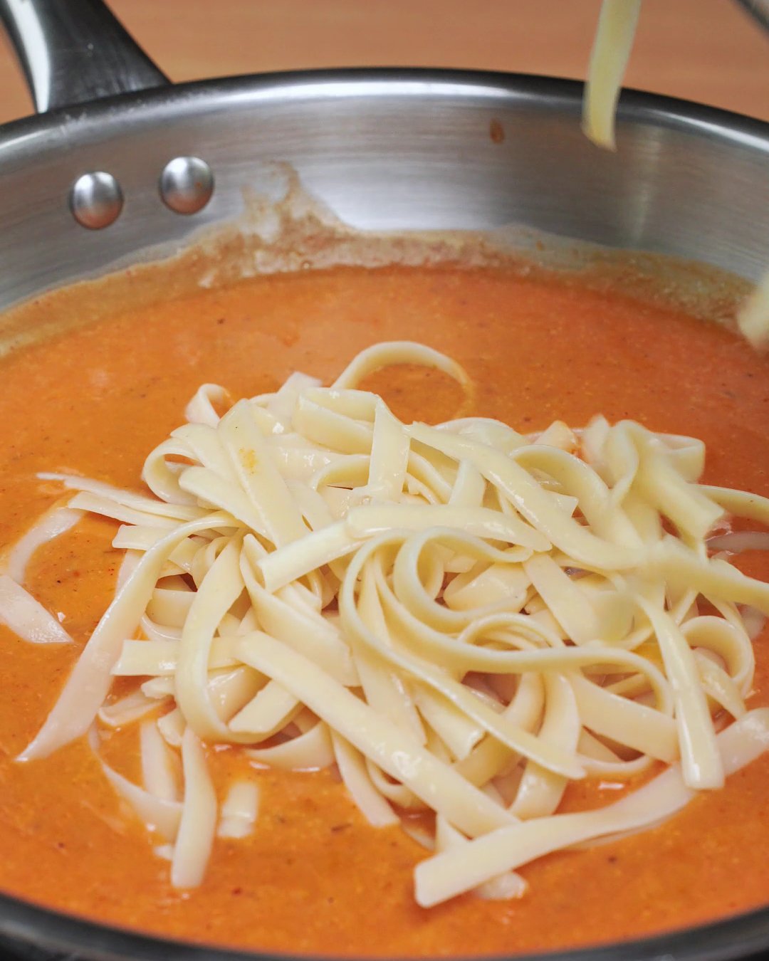 Freshly cooked fettuccine being added to creamy tomato mushroom sauce