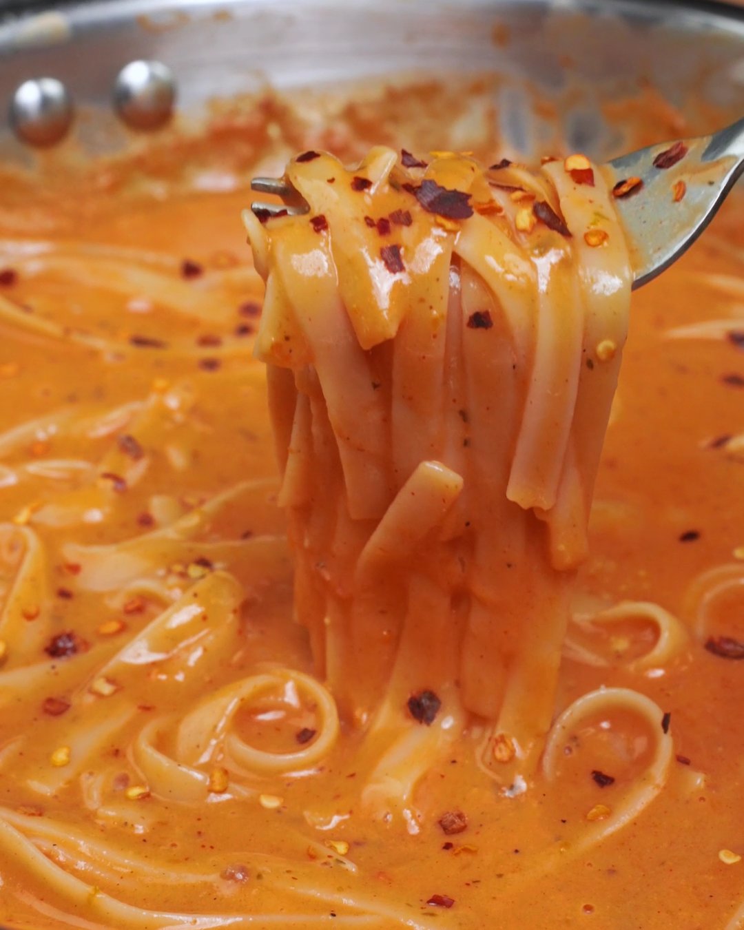 Fettuccine twirled on a fork in creamy tomato sauce with red pepper flakes