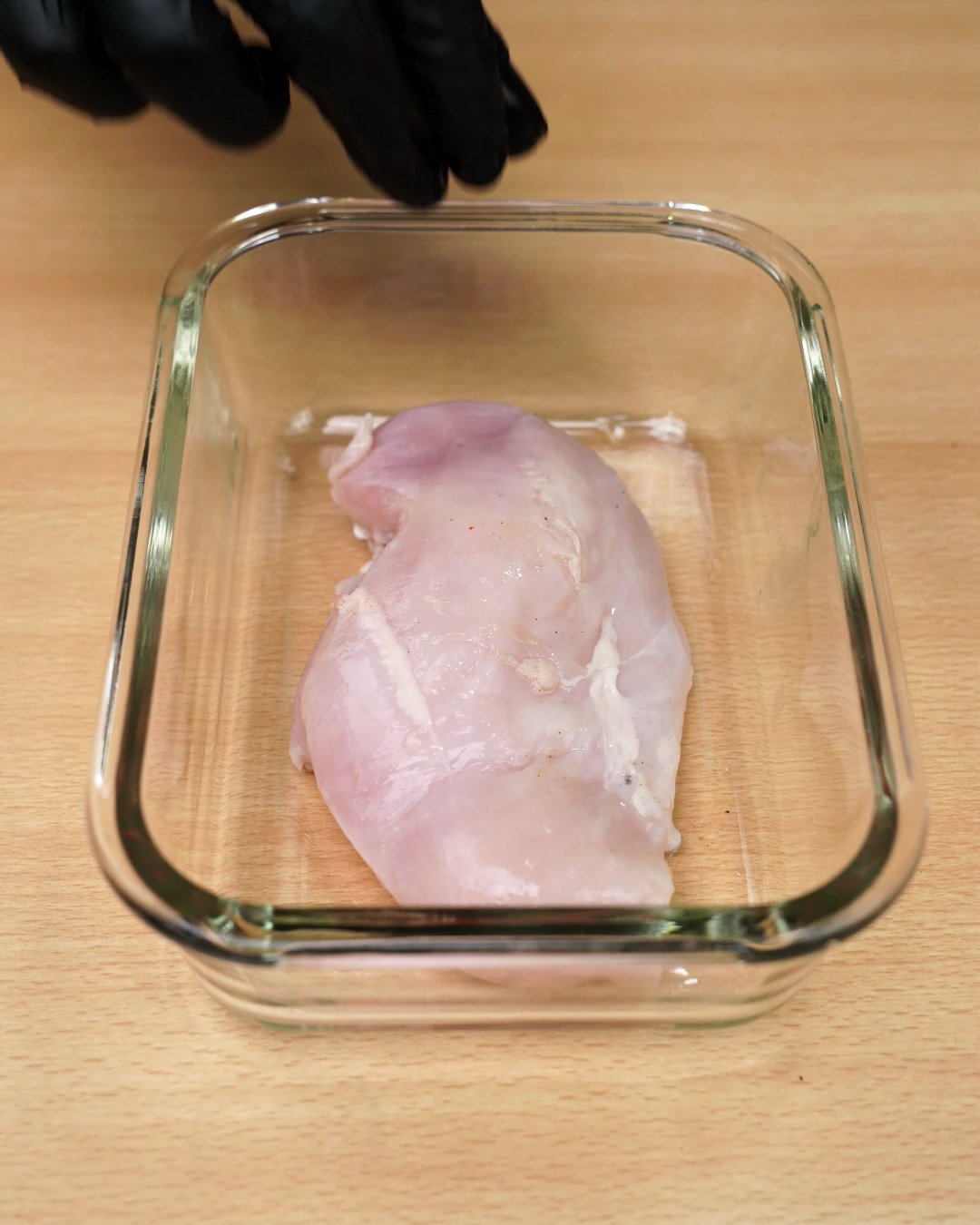 A raw chicken breast in a glass dish