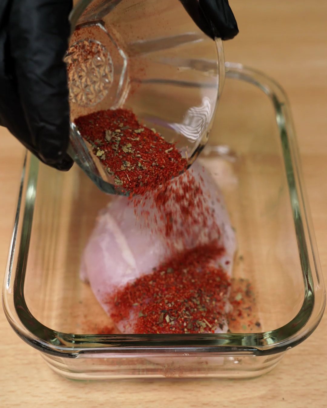 A red paprika spice mix with dried herbs being poured over a chicken breast