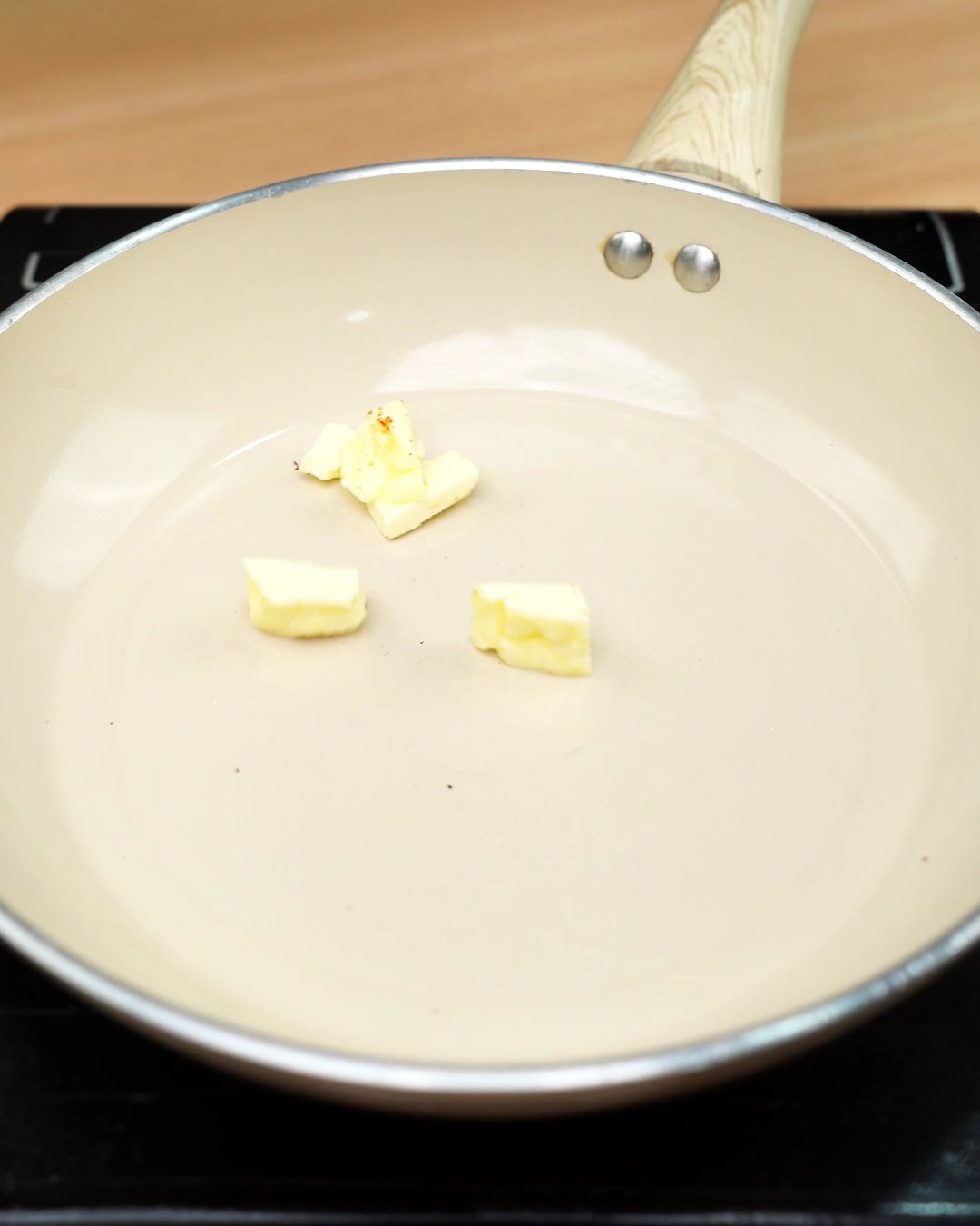 Small cubes of butter melting in a cream-colored skillet